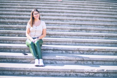 Mutlu ve kendinden emin gülümseyen genç ve güzel bir kadın. Şehrin sokaklarında gülümseyerek merdivenlerde oturmak.