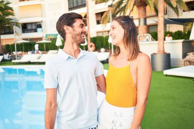 Tatilde mutlu ve kendinden emin gülümseyen genç bir çift. Yüzünde tebessümle plaj kulübünde sarılırken