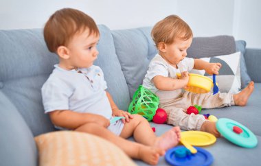 Kanepede oturup evde oyuncaklarla oynayan güzel bebekler.