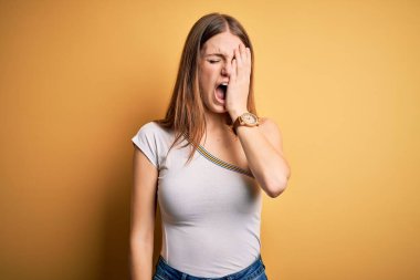 Genç, güzel, kızıl saçlı bir kadın izole edilmiş sarı arka plan üzerine günlük tişört giyiyor. Yüzünün yarısını, gözünü ve ağzını eliyle kapatmaktan yorulmuş. Yüzüm acıyor..