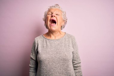 Son sınıftaki güzel bir kadın, günlük tişört giyip pembe arka planda dikiliyor kızgın ve öfkeli çığlıklar atıyor, öfkeyle bağırıyor. Öfke ve agresif kavram.