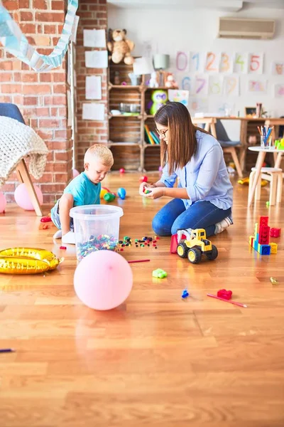 年轻的高加索孩子和老师在学校玩耍 在游戏室的母亲和儿子用玩具块支撑着一座塔 — 图库照片