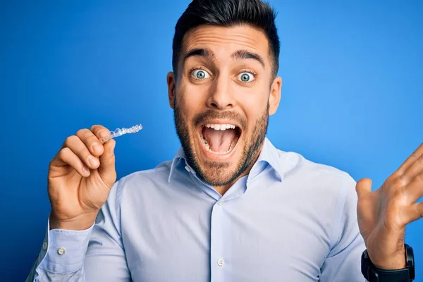 Jovem Homem Bonito Segurando Dente Aligner Correção Sobre Fundo Azul — Fotografia de Stock