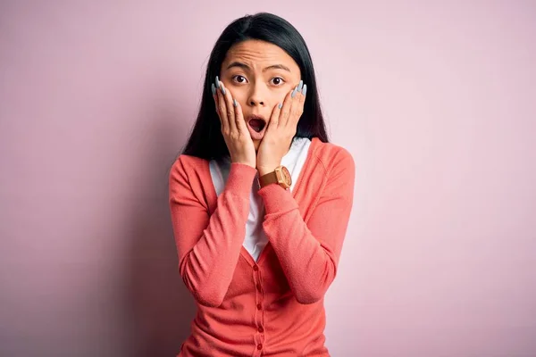 Young beautiful chinese woman wearing casual sweater over isolated pink background afraid and shocked, surprise and amazed expression with hands on face