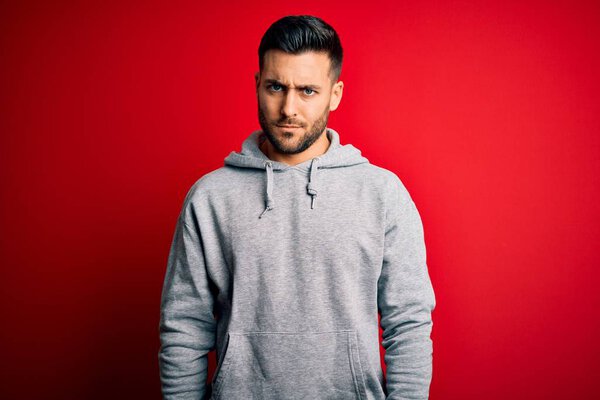 Young handsome sportsman wearing sweatshirt standing over isolated red background skeptic and nervous, frowning upset because of problem. Negative person.
