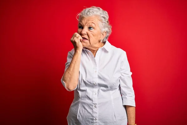 年长的漂亮女人穿着雅致的衬衫站在孤立的红色背景之上 看上去紧张而紧张 双手放在咬指甲的嘴上 焦虑问题 — 图库照片