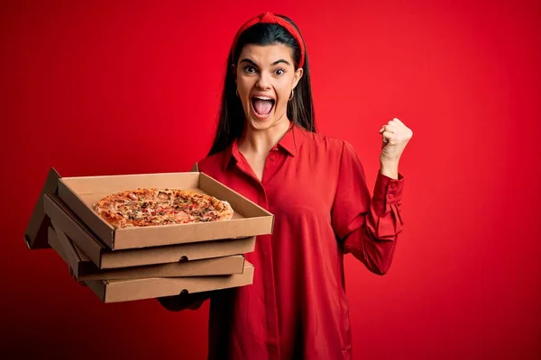 若い美しいブルネットの女性はイタリアのピザと配達箱を持っています赤い背景の上に叫んで誇りと勝利と成功を祝う非常に興奮し 応援感情 — ストック写真
