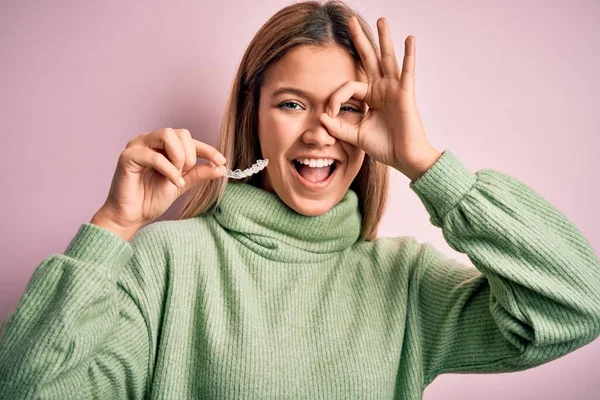 年轻而美丽的女人 手里拿着小饰物 站在孤立的粉色背景上 笑容满面 手拿着手拿着手签 手拿着手拿着手指头看 — 图库照片