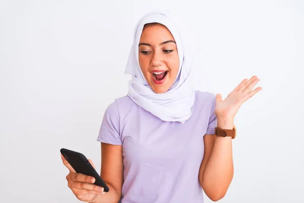 若いです美しいですアラビア語の女の子身に着けていますヒジャーブスマートフォンを使用して隔離された白い背景に非常に幸せと興奮 勝者の式は大きな笑顔で叫んで勝利を祝いますと手を上げ — ストック写真