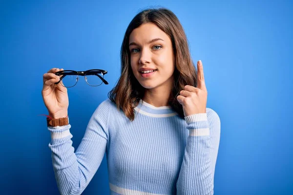 Joven Chica Rubia Sosteniendo Lentes Ópticas Sobre Fondo Azul Aislado — Foto de Stock