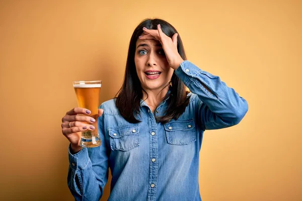 青い目のビールを飲んでいる若い女性が孤立した黄色の背景の上に立って手で頭の上に強調し 恥と驚きの顔で 怒っているとフラストレーションにショックを受けた 恐怖と過ちへの動揺 — ストック写真