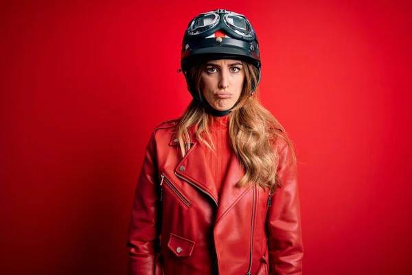 若い美しいブルネットのオートバイの女性は 赤い背景の上に元ヘルメットを身に着けている落ち込んでいると苦痛のために心配し 怒っていると恐れて泣いています 悲しい表情 — ストック写真