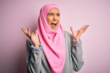 Pembe Müslüman başörtüsü ve iş ceketi giyen genç ve güzel esmer iş kadını deli gibi bağırıyor ve agresif bir ifade ve kolla bağırıyor. Hayal kırıklığı konsepti.