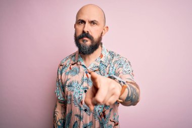 Sakallı ve dövmeli yakışıklı bir adam pembe arka planda sıradan bir çiçek gömleği giyiyor. Kameraya kızgın ve sinirli olduğunu gösteriyor.