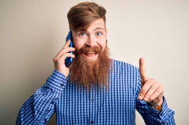 Kızıl saçlı, sakallı İrlandalı bir adam, izole bir arka planda akıllı telefondan konuşuyor. Bir fikir ya da soru işareti ile şaşırmış, mutlu yüzlü, bir numara.