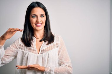 Mavi gözlü genç esmer kadın izole edilmiş beyaz arka plan üzerine gündelik tişört giyiyordu. Büyük ve büyük beden işareti, ölçü işareti gösteriyordu. Kameraya bakıp gülümsüyor. Ölçüm konsepti.