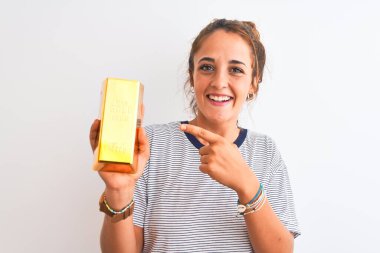 Güzel, kızıl saçlı, altın külçeli genç bir kadın, izole bir arka planda, mutlu bir şekilde elini ve parmağını işaret ediyor.