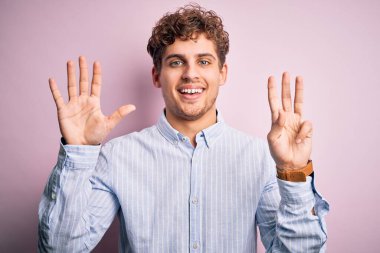 Sarışın, kıvırcık saçlı, beyaz arka planda çizgili gömlek giyen ve 8 numaralı parmaklarıyla işaret eden genç, kendinden emin ve mutlu bir adam..
