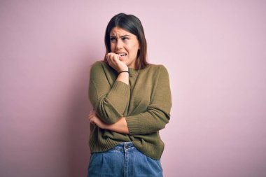 İzole edilmiş pembe arka plan üzerinde sıradan bir süveter giyen genç bir kadın elleri ağız yiyen tırnaklarla gergin ve stresli görünüyor. Endişe sorunu.