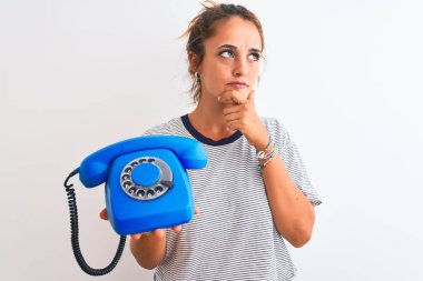 Genç kızıl saçlı kadın klasik retro telefonu izole edilmiş arka planda tutuyor. Ciddi bir yüz. Soruyu düşünüyor, kafası karışık bir fikir.