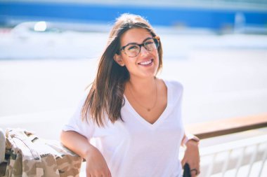 Mutlu ve kendinden emin gülümseyen genç ve güzel bir kadın. Kasaba caddesinde yüzünde gülümsemeyle dikilirken