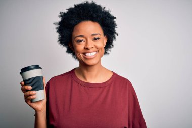 Kıvırcık saçlı, mutlu yüzlü, gülümseyen, kendine güvenen, dişlerini gösteren bir gülümsemeyle bir fincan kahve içen Afro-Amerikan genç kadın.
