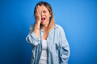 Orta yaşlı, güzel bir kadın, günlük gömleğini giymiş, mavi arka planda dikiliyor, esnemekten yorulmuş, yarı yüz, göz ve ağzı elle kapatıyor. Yüzüm acıyor..