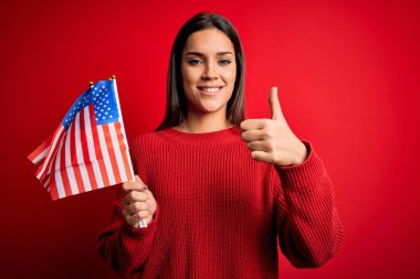 Amerika Birleşik Devletleri bayrağını kırmızı arka planda tutan genç, güzel, vatansever kadın gülümsüyor.