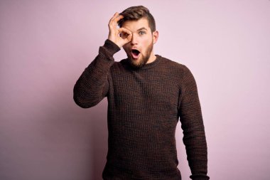 Sakallı ve mavi gözlü genç bir adam pembe arka planda sıradan bir süveter giyiyor. Şok olmuş bir jest yapıyor. İnançsız ifade.