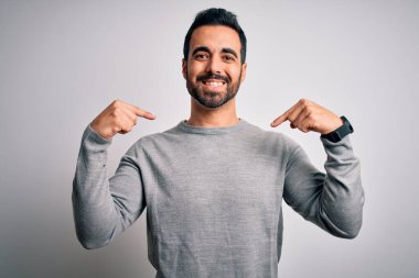 Sakallı, sıradan bir süveter giyen, beyaz arka planda duran, kendine güvenen, kendini gururlu ve mutlu gösteren genç yakışıklı bir adam..