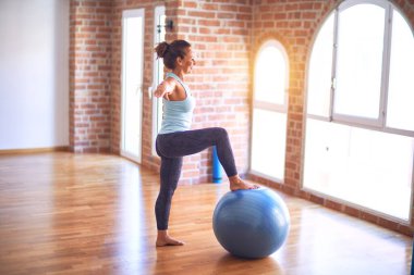 Orta yaşlı güzel sporcu kadın mutlu gülümsüyor. Spor salonunda yoga sınıfında spor topu kullanarak esneme hareketi.