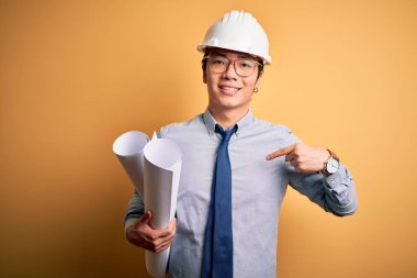 Güvenlik kaskı takan genç, yakışıklı mimar elinde sürpriz yüzüyle kendini gösteren planlar tutuyor.