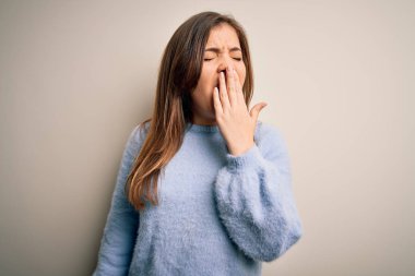 Kış süveteri giymiş güzel bir kadın izole arka planda dikiliyor. Elle ağzını kapatmaktan sıkılmış. Huzursuz ve uykulu..