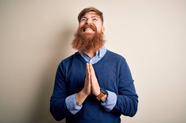 Yakışıklı İrlandalı kızıl saçlı, sakallı bir iş adamı izole edilmiş bir arka planda duruyor, elleri bağlı yalvarıyor ve dua ediyor. Yüzünde umut ifadesi var. Çok duygusal ve endişeli. Yalvarıyorum..