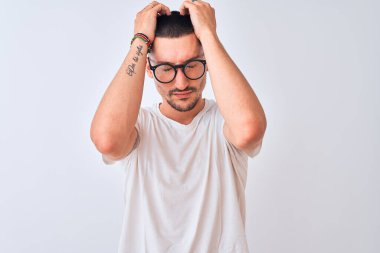 Gözlük takan ve izole edilmiş arka planda duran genç yakışıklı adam acı ve migrenden dolayı çaresiz ve stresli bir baş ağrısı çekiyor. Ellerini başının üstüne koy..