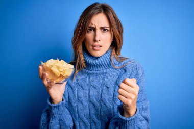 Elinde patates cipsi olan genç, güzel esmer bir kadın. Sinirli ve sinirli bir şekilde bağırıyor. Öfkeyle bağırıyor.