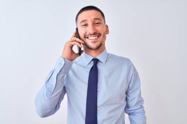 Genç yakışıklı iş adamı, izole edilmiş arka planda akıllı telefon kullanarak arıyor. Mutlu bir yüzü var, gülümsüyor ve kendine güvenen bir gülümsemeyle dişlerini gösteriyor.