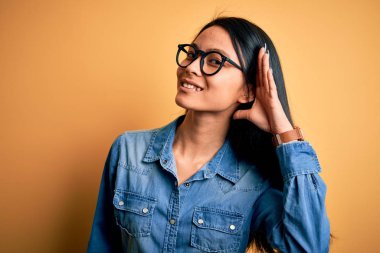 İzole edilmiş sarı arka planda rahat bir kot gömlek giyen genç, güzel Çinli bir kadın kulağından girip kulağına gelen dedikoduları ya da dedikoduları dinliyor. Sağırlık kavramı.