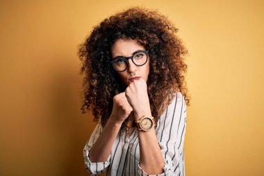 Kıvırcık saçlı, piercingli, çizgili gömlekli, gözlüklü savunma hareketleriyle dövüşmeye hazır kızgın ve üzgün yüzlü sorunlardan korkan genç bir kadın.