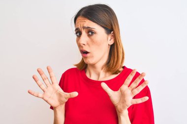 Güzel kızıl saçlı kadın, izole edilmiş arka planda günlük kırmızı tişört giyiyor. Korkudan dehşete düşmüş ve korkmuş. El hareketlerini durdur, şok içinde bağır. Panik konsepti.