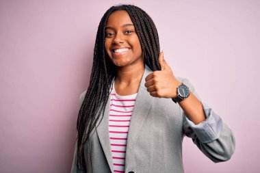 Genç Afro-Amerikalı iş kadını pembe izole edilmiş arka planda durup mutlu bir el hareketi yapıyor. Kameraya bakıp başarıyı gösteren ifade onaylanıyor.