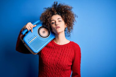 Kıvırcık saçlı, piercing takan, müzik dinleyen, kendine güvenen, zeki yüzlü, kendine güvenen bir radyo kullanan genç ve güzel bir kadın.