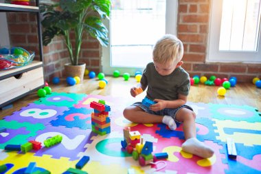 Anaokulunda oyuncak bloklarıyla oynayan beyaz bir çocuk. Anaokulu çocuğu oyun odasında kule inşa etmekten mutlu.