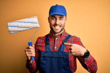 Genç yakışıklı ressam duvarları boyuyor. İzole edilmiş sarı arka plan üzerinde yuvarlanıyor. Yüzü kendini gösteren sürpriz bir yüz var.