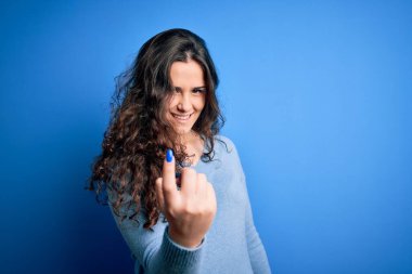 Kıvırcık saçlı, mavi süveter giyen, izole edilmiş arka planda genç ve güzel bir kadın seni buraya davet ediyor.