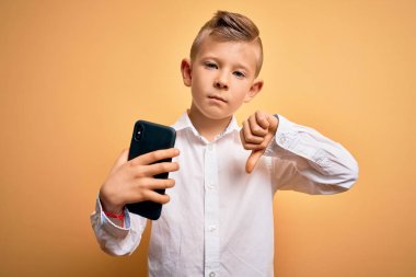 Küçük beyaz bir çocuk akıllı telefon kullanıyor ve kızgın yüzüyle telefonun ekranına bakıyor. Negatif işaret baş parmakları aşağıda, reddedilme konsepti ise...