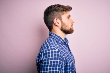 Sakallı, mavi gözlü, sıradan tişörtlü, yan yana duran yakışıklı sarışın, rahat bir poz veren, kendine güvenen bir gülümsemesi olan genç adam..
