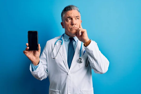 中年英俊 白发苍苍的医生拿着智能手机 脸上露出严肃的表情 思考着问题 非常迷惑的想法 — 图库照片