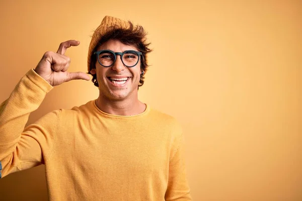 孤立した黄色の背景にカジュアルなTシャツと眼鏡を身に着けている若いハンサムな男は笑顔と指を見て カメラと小さなサイズの看板を行う手で自信を持ってジェスチャー 概念の測定 — ストック写真