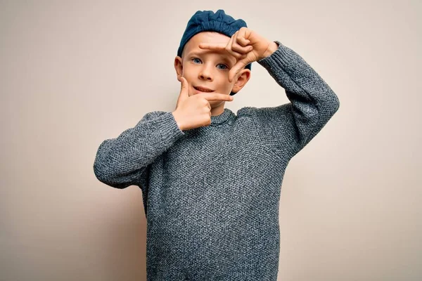 青い目の若い白人の子供は 孤立した背景にウールキャップを身に着けており 幸せな顔をした手と指でフレームを作っています 創造性と写真の概念 — ストック写真